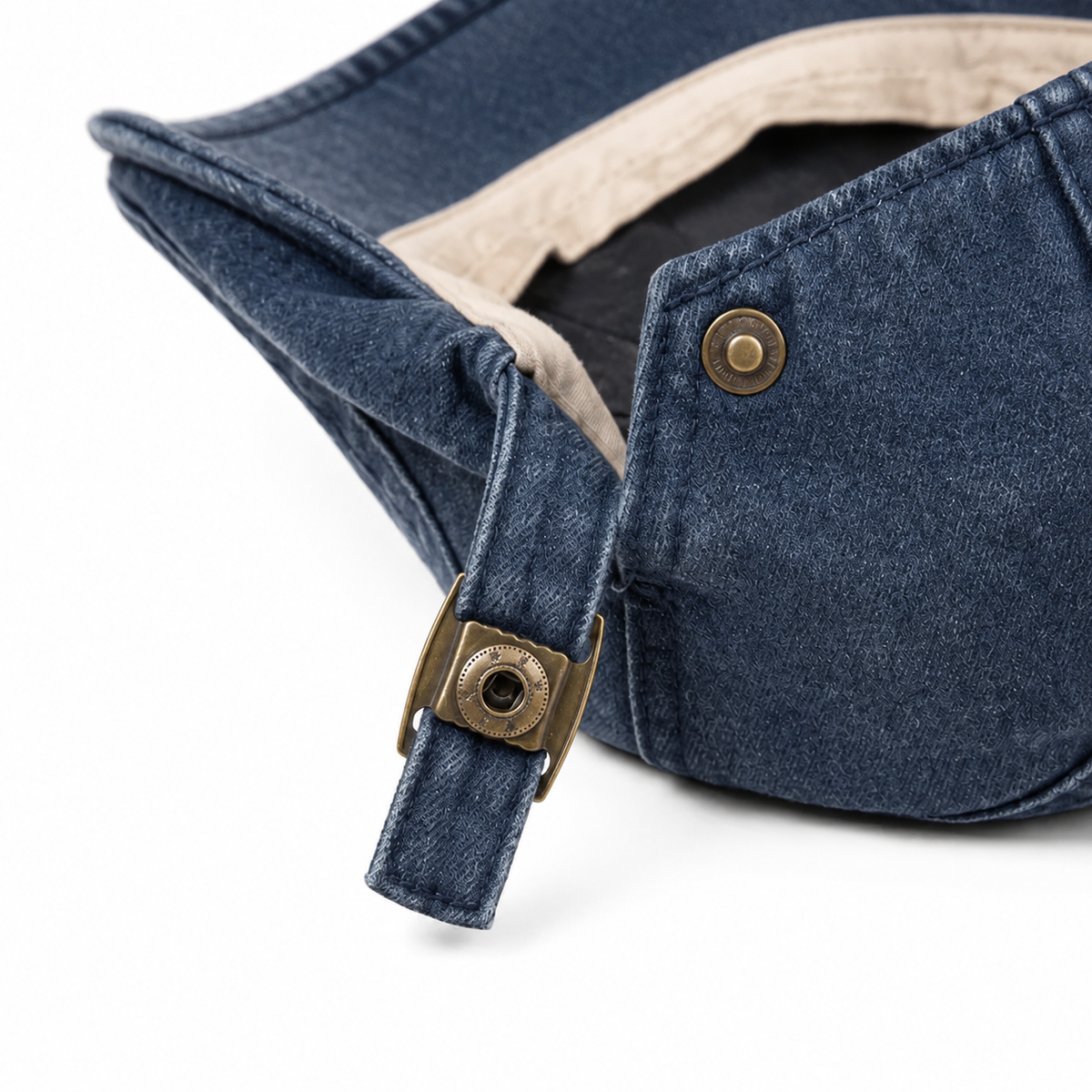 Close-up of the Denim Blue vintage flat cap interior, adjustment strap and brass hardware on a white background